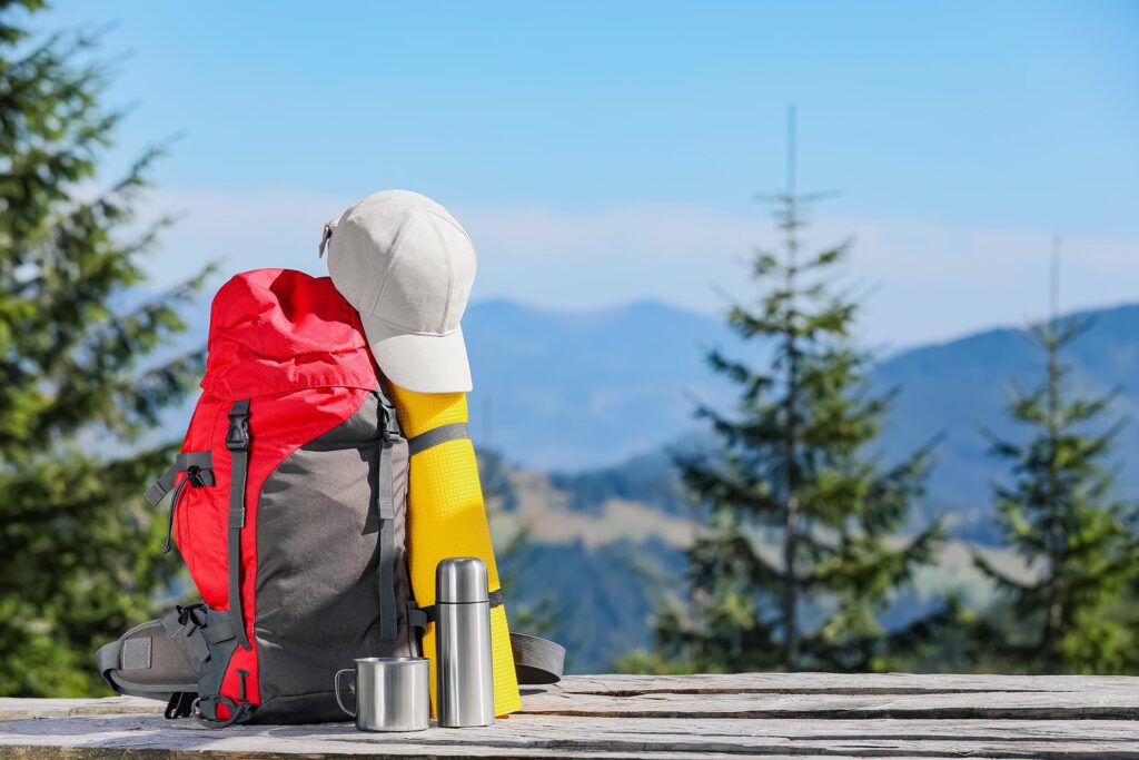 Backpack and other camping gear on wooden surface outdoors, space for text. Mountain tourism; Shutterstock ID 2050691000; other: -; purchase_order: -; client: -; job: -